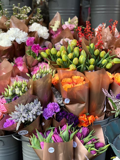 An array of fresh flowers displayed in buckets, featuring various colors and types suitable for floral gift arrangements or flower delivery. In the foreground, there are pink tulips with green stems a
