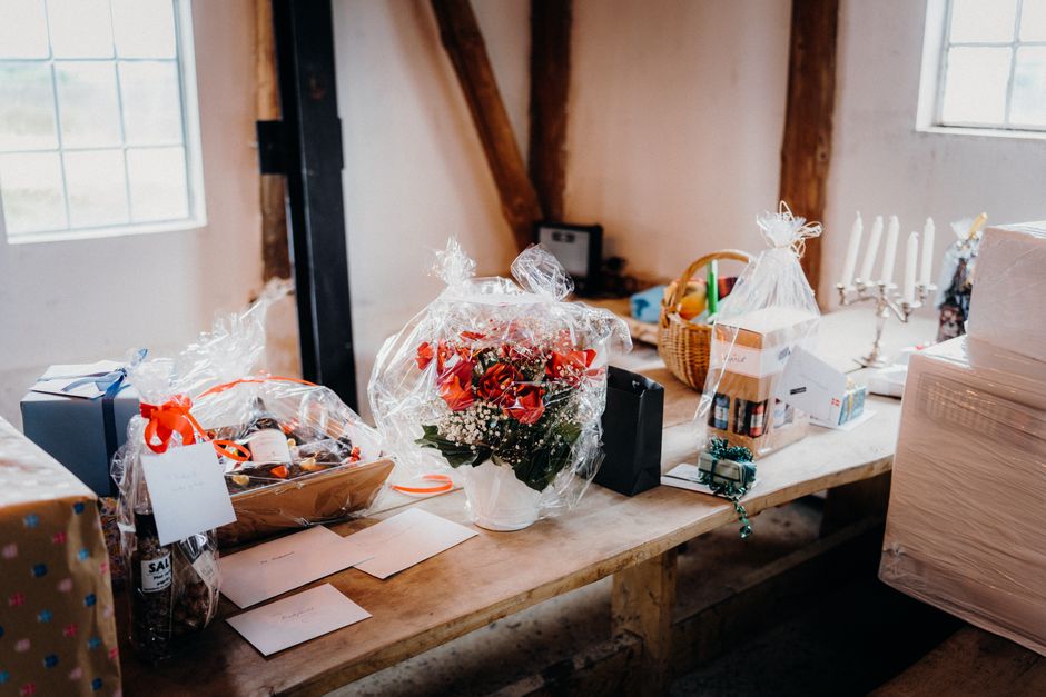 A fresh floral bouquet featuring vibrant red roses, white baby's breath, and green foliage, wrapped in clear cellophane and tied with a decorative ribbon, resting on a wooden table alongside various w