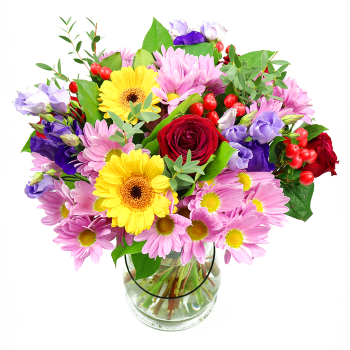 In this image, a lush, overflowing bouquet stands in a simple clear glass vase, the white background allowing every bloom to shine with the clarity of a bright day over East Dulwich's tree-lined streets. The centre of the arrangement is defined by velvety deep red roses, their petals layered in tight spirals that speak of romance and enduring affection. Just beyond them, bold yellow gerbera daisies with dark brown-orange centres stretch their daisy-like faces outward, radiating warmth and positivity, like cheerful splashes of sunshine. Around this core, generous heads of pink chrysanthemums and daisy-style flowers form a soft, pastel collar; each bloom is made up of many slender petals circling tiny yellow centres, adding a feathery volume that feels both comforting and abundant. Woven gracefully throughout, purple and lavender lisianthus introduce cooler tones and an elegant, bell-shaped silhouette, their slightly ruffled edges bringing a refined, almost poetic note, as if reflecting the creative, village-like character of East Dulwich. Bright red hypericum berries punctuate the arrangement in small clusters, their smooth, round shapes and glossy finish providing a playful counterpoint to the velvety roses and the fluffy daisies. The bouquet is framed and supported by a variety of green foliage: sturdy, dark green leaves sit close to the stems, while lighter, more delicate sprigs extend outward, giving a sense of movement and natural growth. Inside the clear vase, the neatly cut stems are visible through the water, showing the care and precision behind the design. The overall feel is joyous yet composed, the kind of bouquet you might have delivered to celebrate a new arrival, a birthday, or a special gathering in a home near Goose Green.